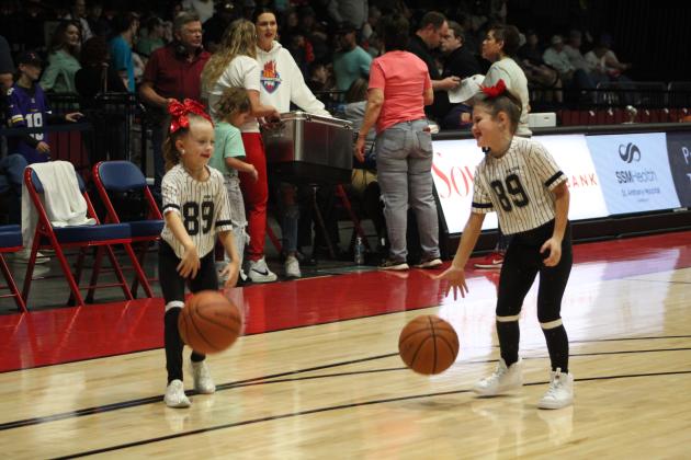 Two girls on the Sparklers Dance Team, Taiyn Masoner, 7, of Tecumseh, left, and Bristol Lane, 8, of Prague, take to the court to practice their basketball skills during halftime of the Potawatomi Fire home game on March 25. Their mothers, in white shirts in the background, tied to win a cooler in the "Knockout" contest, making the most straight baskets. They are Lindsay Lane, who played basketball at Konawa High School, and Audrey Masoner, who played for Tecumseh High School and St. Gregory's University.