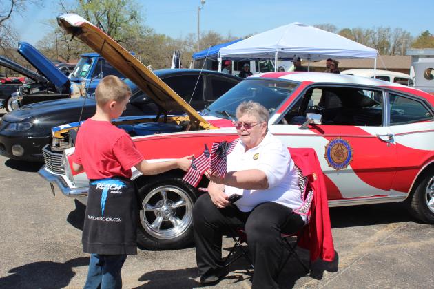Donna Snodgrass, president of Tecumseh Post 260 American Legion Auxiliary, hands a flag to Jaxon Prince, 11, of Bethel, during the 7th Annual Bethel Band Boosters Car Show on April 8. Countywide &amp; Sun/Natasha Dunagan