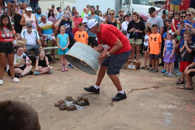 Kiwanis Club volunteer Brad Mauldin releases turtles from under a metal tub for the turtle races, as their owners and parents watch during the McLoud Blackberry Festival on July 8. They also had sack races, balloon toss, money in the hay and a duck pond for kids. Countywide &amp; Sun/Natasha Dunagan