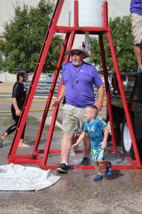 Retired Rural Fire Coordinator Paul Simpson emerges from the cold water flowing from the Bucket Brigade barrel, with Legend Walton, 4, of Shawnee. Simpson continued to organize the Firefighter Olympics at the Pottawatomie County Free Fair this year. Teams from Tecumseh, Asher and Prague participated in the event, and Prague won on Sept. 9. Countywide &amp; Sun/Natasha Dunagan