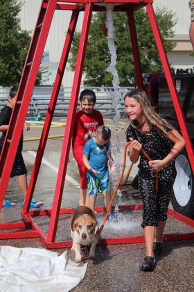 Grace Holmes, 10, of Asher, leads her beagle Rocko through the draining water from the bucket brigade barrel - as Legend Walton, 4, of Shawnee, enters the stream - during the Firefighter Olympics on Sept. 9. Countywide &amp; Sun/Natasha Dunagan