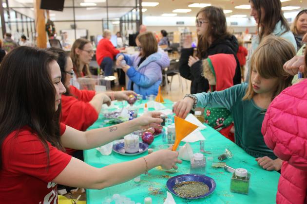Shawnee Pioneer Library employee Noelani Sogata holds a funnel as Charlotte McGee, 6, of Shawnee, adds glitter to the inside of a clear ornament during the Shawnee Tree Lighting event on Nov. 17. Attendance was so high that the library was running out of craft supplies. Countywide &amp; Sun/Natasha Dunagan