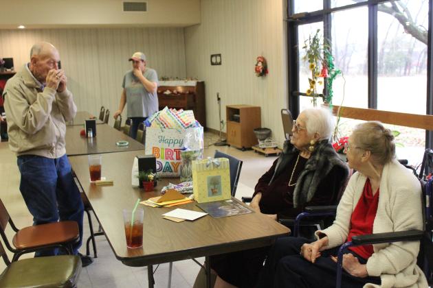 Ed Medcalf, age 93, plays a harmonica his grandmother gave him at age 6, and sings “Have I Told You Lately That I Love You,” to his friend Clemmie Lucas during her early 100th birthday party on Dec. 15. Lucas will turn 100 on Christmas Day, and Project H.E.A.R.T, in conjunction with the Tecumseh Senior Center, hosted her birthday party. Also shown, far right, is Lucas’s friend, Charlotte Harrison. Countywide &amp; Sun/Natasha Dunagan