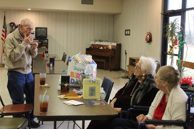 Ed Medcalf, age 93, plays a harmonica his grandmother gave him at age 6, and sings “Have I Told You Lately That I Love You,” to his friend Clemmie Lucas during her early 100th birthday party on Dec. 15. Lucas will turn 100 on Christmas Day, and Project H.E.A.R.T, in conjunction with the Tecumseh Senior Center, hosted her birthday party. Also shown, far right, is Lucas’s friend, Charlotte Harrison. Countywide &amp; Sun/Natasha Dunagan