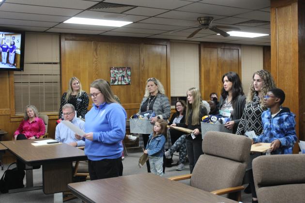 SHS FFA Advisor Jordan Miller reads a speech by Shawnee FFA President Hope Sitton, as administrators and students wait to present gifts to the school board.