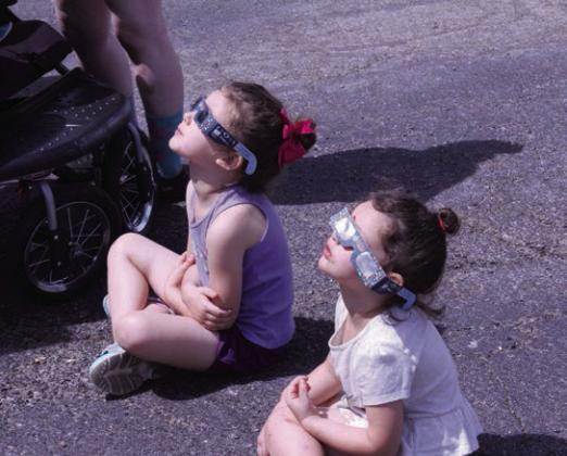 Mavis Lucas, 5, and River Lucas, 3, both of Tecumseh, sit in the Tecumseh Pentecostal Church of God parking lot wearing their solar eclipse glasses to watch the show in the sky. The Tecumseh Public Library provided the glasses, as well as Moon Pie and Star Crunch snacks.
