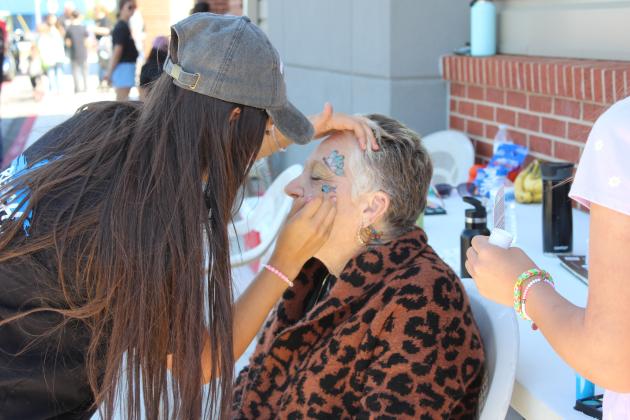 Chenoa Ladra of Reach Church paints butterflies on the face of Tonda Sterrett of Tecumseh, who is a fellow church member, during the Eighth Annual Bethel Band Boosters Car Show Fundraiser on April 13. Reach Church also made and sold funnel cakes and had a bounce house during the event. Countywide &amp; Sun/Natasha Dunagan