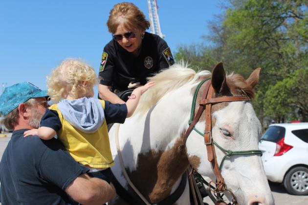 Noah Neely, 3, of Shawnee, is held by Richard Neely, as he pets Princess the paint horse during the Touch a Truck and Beyond event on April 6. Atop Princess is Detective Jan Montgomery of the McLoud Police Department, who points out the soft mane. Montgomery was at the event with her husband, Roger Montgomery, a crime scene investigator at MPD who rode Dollar. The horses are used for parades and other events, and R. Montgomery said they hope to begin patrolling Wes Watkins Reservoir with them, as well..
