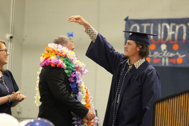 Asher graduate Jordyn Litson adds another silk flower to Principal Steve Spangler after all the graduates bestowed him with leis before receiving their diplomas on May 11. Asher's commencement included 13 graduates. Countywide &amp; Sun/Natasha Dunagan