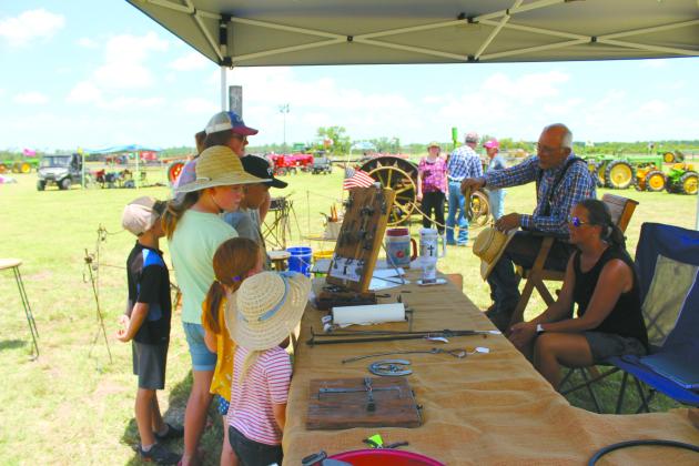 Members of the Ramsey family from Macomb visit with blacksmith Tom Nelson, of Douglas, and his daughter Karrah Cronister at their booth in the 25th Annual Farming Heritage Festival at Shawnee Feed Center on June 22. Countywide &amp; Sun/Natasha Dunagan