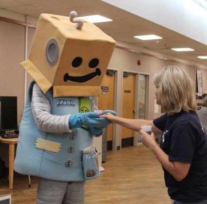 Tinker Federal Credit Union Community Engagement Representative Tina Harman hands "Save-A-Tron" the SaveAbles Kids Club robot a smoothie made by the 4-H Club blender bike at the Shawnee Library's Blast-off to Learning event on May 30. Countywide &amp; Sun/Natasha Dunagan