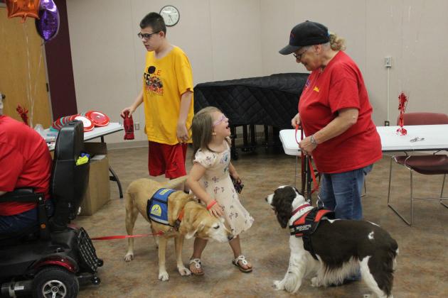 EmmaLeigh Claxton, 5, of McLoud, has a laugh with Debi Christian with the Volunteers in Police Service (VIPS), as she pets service dogs Frolic and Bridgette, and Lincoln Claxton, 14, looks over the VIPS booth at the Shawnee Library's Blast-off to Learning event on May 30. Countywide &amp; Sun/Natasha Dunagan