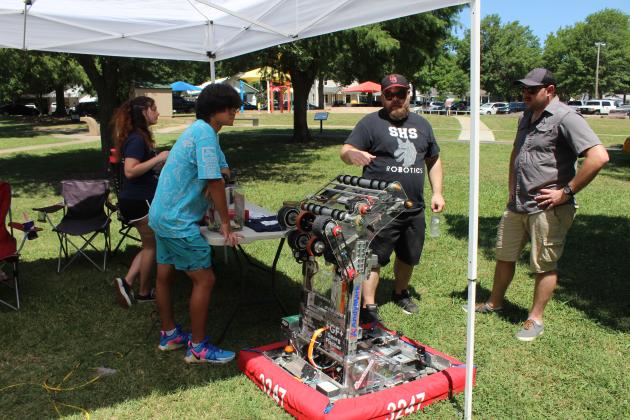 Shawnee Robopack Coach Cullen Birney, third from left, talks with former SHS robotics student Justin Kannenberg about their latest robot which can retrieve and shoot foam rings. The Robopack, including junior Lillie Lackey and sophomore Jun Gao, had a booth at the 37th Annual Knights Auto Club Car Show, June 22, and were selling tickets for a 50-50 pot to help fund the program. Birney said Randy Schultz is their engineer and assistant coach, and he had a car in the event. Countywide &amp; Sun/Natasha Dunagan