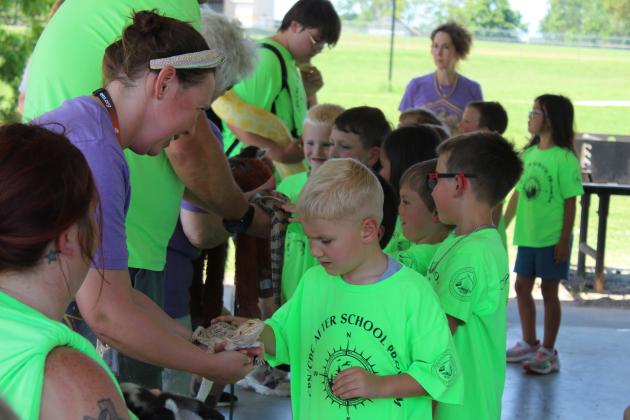 Isaac Sitton, who is in the CPN/CDC After School Program, pets Tank the Bearded Dragon, held by Tecumseh Pioneer Library staff member Aaryn Wasielewski on June 13. About 35 children came from the CPN program to Slick Humphrey Park for the library's Summer Learning Challenge Extreme Animals program. Keeley Knowles, a handler with Extreme Animals in Tuttle, spoke about the bearded dragon, blue-tongued skink, albino Burmese python, armadillo, hedgehog and two lemurs before the children lined up.