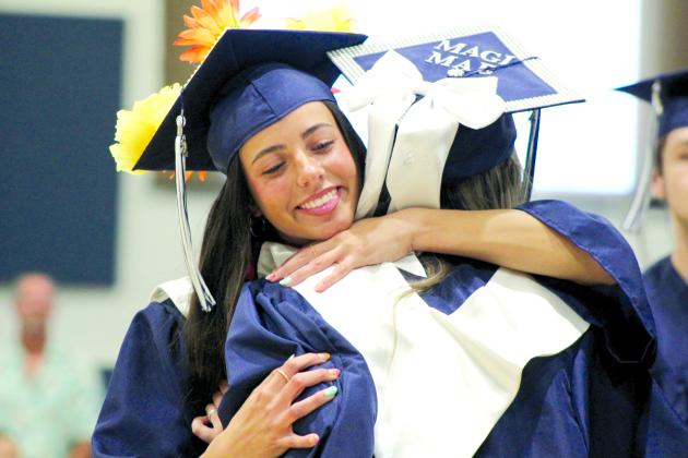 Graduates Payton Leba and Magi Melton exchange flowers and hugs at graduation on May 11. Leba was the Class of 2024 Valedictorian. Countywide &amp; Sun/Natasha Dunagan