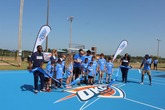 Bethel Mayor Tony Carlile cuts the ribbon on the newly-resurfaced Bethel Community Court, as children from the community and members of the OKC Thunder Cares program watch on July 15. The emcee for the event was Malcolm Tubbs, far right, who is with the Thunder. They also brought a three-member drum corp. Countywide &amp; Sun/Natasha Dunagan