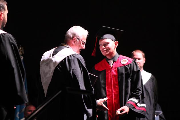 An NRC graduate hands Principal Chad Brooking a power ball before receiving his diploma.