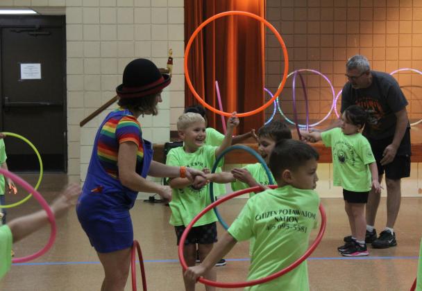 Chelsea Parks, from the Inspyral Circus, shows Owen Trout how to spin a hula hoop on his arm during the Summer Learning Challenge program at Tecumseh Pioneer Library on July 11. Also shown are Isaac Sitton, background, and Luke Hohn, foreground. The theme of the program was "practice makes progress," as Parks demonstrated other circus skills like juggling, riding a unicycle, and balancing on a rola bola and a giant rubber ball. The next children's program is "Cinderella Interactive - A Literary Tale."