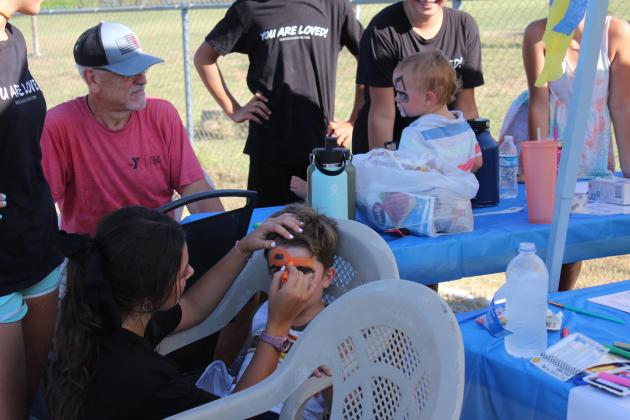 Chenoa Ladra paints a truck on the face of Zebulon Brackett, 3, of Shawnee, at the Reach Church booth during the Bethel High School Blue &amp; Gold Bash at the football field on Aug. 17. Boaz Brackett, 1, is shown with his face painted, as well. Church members also gave away popcorn. Countywide &amp; Sun/Natasha Dunagan