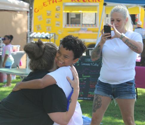 Exzavier Beal, 7, of Shawnee, hugs his mom, Kayla Beal, to make a "Forever Hug" with his arms painted white and hers blue during the First Annual Hug-A-Thon held at Woodland Veterans Park on Aug. 3. Also shown, recording the moment, is Exzavier's aunt, Rita Beal. Countywide &amp; Sun/Natasha Dunagan