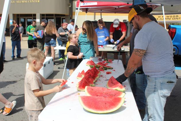 Jaden Neal, 7, of Shawnee, takes a slice of watermelon, as Steven Self prepares to cut more at the Mission Tecumseh Back to School Bash, held at the WP Wood/THS Alumni Center on July 27. Lang Bartmess (behind Self) brought about 10 watermelons for the event. In the neighboring tent, Nicki &amp; Shane Mills assemble and wrap around 500 hotdogs. There were also free snow cones that attracted a long line, and inside the building they provided school supplies and backpacks. Countywide &amp; Sun/Natasha Dunagan