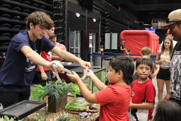 Paxton McKenzie, with Extreme Animals, hands a Speckled King Snake to Waylon Meeks, 9, as Weston Meeks, 7, looks on and his dad, Gunner Meeks, all of Tecumseh, watches at the Pitt Stop Petting Zoo during the Outdoor Network Expo at FireLake Arena on Aug. 9. Countywide &amp; Sun/Natasha Dunagan