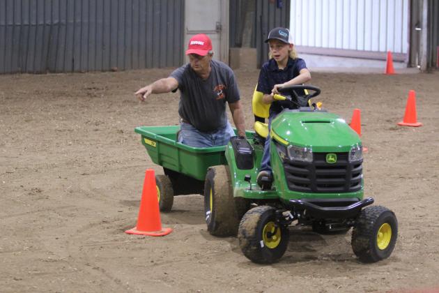 Dace Dockrey, age 9, drives a garden tractor through the obstacle course of the Peewee and Midget Tractor Operator Contest, as Fair Board Member Lynn Marlow, points to where he needs to go, on Sept. 6 at the Pottawatomie County Free Fair. Countywide &amp; Sun/Natasha Dunagan