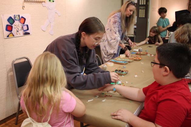 Mabee-Gerrer Museum of Art volunteer Kadence Jenkins ties a scarab bracelet for William McKee, 8, of Shawnee, as Zoe Miller, 7, also of Shawnee, looks on, during Mummy Day at the museum on Oct. 26. Countywide &amp; Sun/Natasha Dunagan