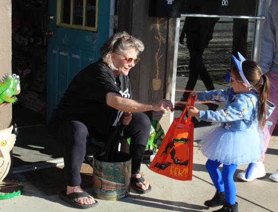 Make It Yourself Owner Leslie Ferrin adds a piece of candy to the bag of Everley Morton, 4, of Tecumseh, during the Tecumseh Business Trick or Treating on Oct. 31. Countywide &amp; Sun/Natasha Dunagan