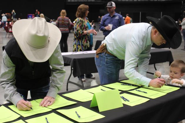 Steve Carpenter, of Dance Creek Beefmasters in Tecumseh, left, and Gus Hull, of Tecumseh Vet Clinic, place their bids at the Silent Trophy Auction during the Pottawatomie County Junior Livestock Show Pig Roast, held at FireLake Arena on Feb. 3. Hull had some help from his son, Taos Hull, age 2. Countywide &amp; Sun/Natasha Dunagan