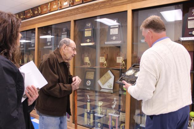 Rev. Scott Hamilton shows a recent trophy to Coach Murl Bowen. Asher High School has added to their trophy cases and organized trophies. They lack state trophies from the 1960s and are hoping alumni will donate them.