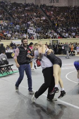 After winning her match on March 1, McLoud freshman Carli Sisco gets a hug from 2024 graduate and girls wrestling alumni Paisley Erskine, who has been helping with the program, and congratulations from Head Coach William Winters. Sisco is the first girls wrestling state champion at McLoud, followed by junior Launa Troutt later that day. Photo provided by Coach William Winters.