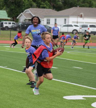 Shawnee High School football player Garrett McCurdy cheers on Collin Beck as he heads to the end zone during a flag football game and Dillon Beck looks on, at the Shamiel Gary Football Clinic for elementary students on May 29 at Jim Thorpe Stadium in Shawnee. There were more than 40 children in this clinic, sponsored by Pottawatomie Go (POGO) for Health Week, and there were over 20 middle school students in the second football clinic that day.