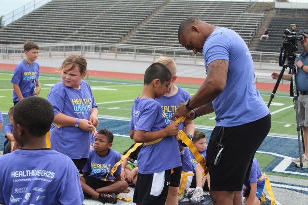 Former NFL safety Shamiel Gary helps an elementary student suit up for flag football during his first of two football clinics on May 29 at Jim Thorpe Stadium in Shawnee.