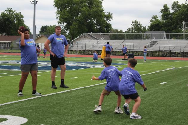 Shawnee High School football player Teddy Jackson throws as two elementary players practice catching/blocking a pass, and Jackson's teammate Kaden Bramlage watches, during the first of two football clinics led by former NFL safety Shamiel Gary, on May 29 at Jim Thorpe Stadium in Shawnee.