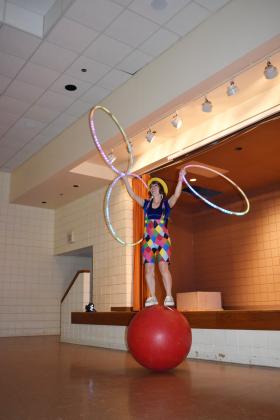 "Hooplahoma" Chelsea Parks, of the Inspyral Circus, balances on a ball and juggles hoops at the Tecumseh Public Library on June 12. Parks demonstrated her circus skills and taught a crowd of children.