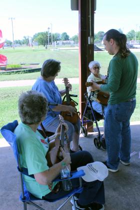 Aaron Pence, with the Norman branch of Pioneer Library System, instructs Carolyn McGraw, Mary Hightower and Barbara Harrison during the "Get Moving: Walk the Park" event with Tecumseh Public Library on June 24 at Slick Humphrey Park. Pence had about six pupils for the ukulele lesson and also shared his percussion instruments.