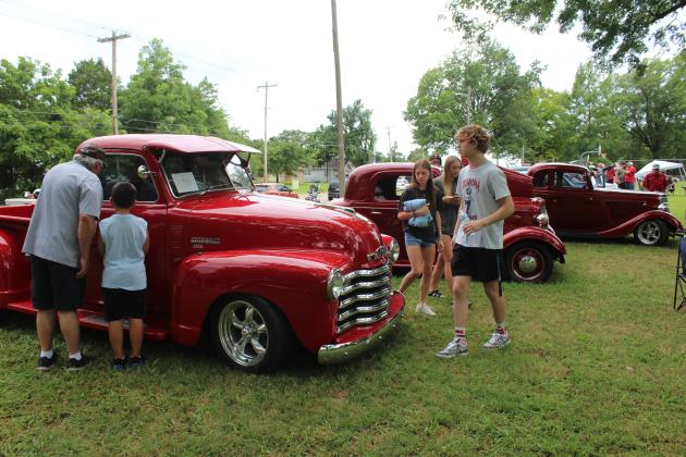 Young and old enjoy the 38th Annual Knights Auto Club Car Show at Boy Scout Park in Shawnee on June 28. These three red vehicles include, far left, a 1950 Chevy Pickup owned by Santos Charriz of McLoud. The event featured 203 entries and 11 club cars, said Lisa Schultz with the Knights in an email.