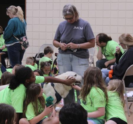 Kary Ann Truitt helps with twisting rubber bands to make feet on someone's "Muttigree" buddy, as children with the CPN Afterschool Program pet Maggie, the seven-year-old Lab mix, during the Tecumseh Public Library program on July 17. Truitt and presenter Ronda Cooper are from the Jasmine Moran Children's Museum in Seminole and are certified as a therapy dog team. They brought craft kits for all of the children to make "Muttigree" buddies.