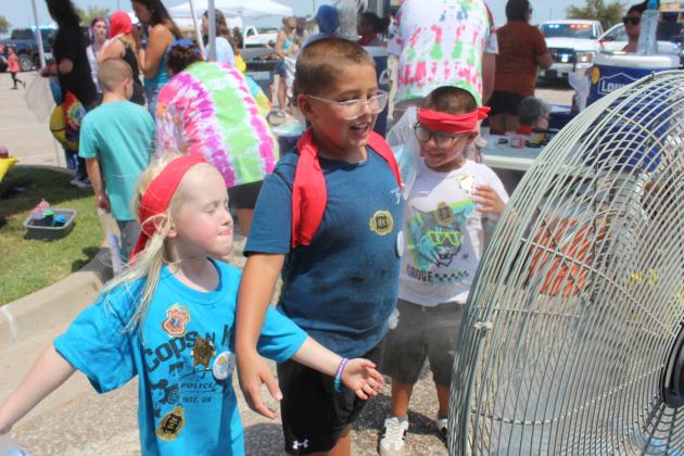 Elinor Peters, 5, Izaiah Peters, 8, and Zaden Peters, 7, all of Shawnee, cool off in front of a misting fan beside the Vision Bank tie-dye tent at Cops N' Kids on Aug. 23. See full cutline below.