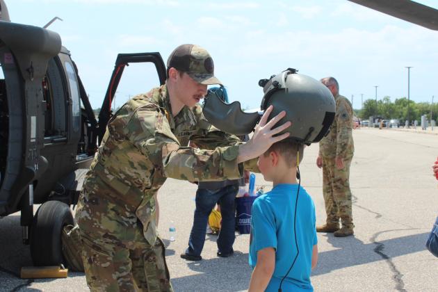Sgt. Justin Donwerth places his helmet on Eli Martin, 8, of Shawnee, during Cops N' Kids on Aug. 23. Children could also sit in the Oklahoma Army National Guard Blackhawk UH60, in background, which flew into Shawnee out of Tulsa.