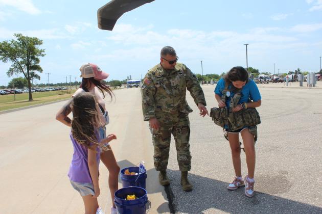 Oklahoma Army National Guard Pilot William Shufeldt talks about his vest with several pockets for supplies, as Bailee Farmer, 11, tries it on, during Cops N' Kids on Aug. 23. Also shown are Hadlee Farmer, 9, and Kayla Farmer, all of Shawnee. Shufeldt and two other soldiers flew their Blackhawk UH60 into the Heart of Oklahoma Expo Center from Tulsa.