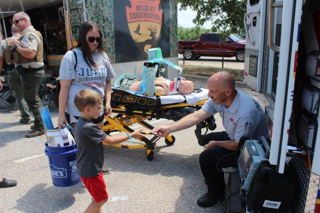 Shawnee REACT Operating Manager James Hulvey hands a sticker to Colter Hardin, 5, of Tecumseh, as Shannon Hardin watches during Cops N' Kids on Aug. 23. Hulvey also demonstrated the Lucas Device, in background, with artificial chest compression and a portable ventilator for oxygen.