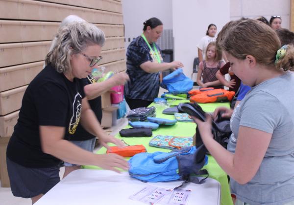 Mission Tecumseh President Brandi Burks, right, along with Cricket Trammell (hidden), and Kathryn Webb, give out backpacks during Mission Tecumseh's 11th Annual Back to School Bash at the W.P. Wood Alumni Center on July 26.