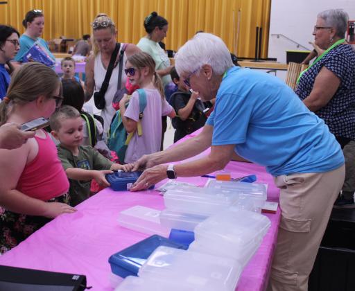 Susan Tischer, right, hands a boy going into preschool a pencil box with dry erase markers during Mission Tecumseh's 11th Annual Back to School Bash at the W.P. Wood Alumni Center on July 26.