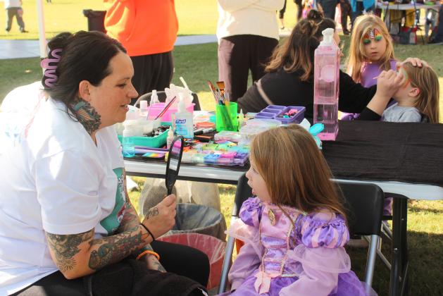 Jessica Flick, owner of Little Bunny Paint n' Things, shows Emma Townley, 6, of Shawnee, the butterfly painted on half her face during the Shawnee Fall Festival at Woodland Veterans Park on Nov. 1. Meanwhile, Gabby Belasco, in the background, paints a rainbow on another girl.