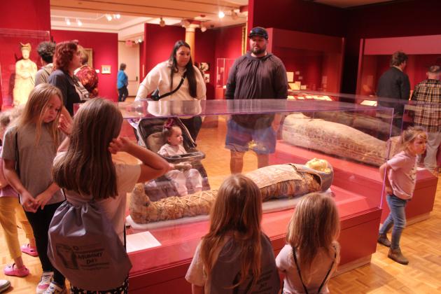 Delayna Trim, Mabee-Gerrer Museum of Art Curator of Collections, at the far left corner of the glass case, answers questions as children and parents view Egyptian mummy Tutu during the Fifth Annual Mummy Day, Nov. 8. There were about 917 visitors to the museum that day, according to Director of Development Sylwia Partyka. For more information on the Egyptian collection, visit https:// www.mgmoa-gallery.com/ .