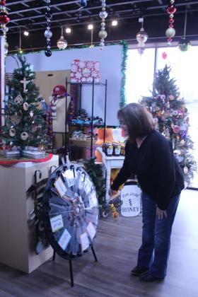 Gayla Roberts of Prague spins the prize wheel and wins a wooden spoon with a wood-burned design at the Okie Dokie Mercantile Ninth Anniversary event in Shawnee on Nov. 28. There were also samples of chocolate, chocolate-covered gummie bears, gourmet salsa, pecan oil and jelly all from Oklahoma companies. Plus, there are five Christmas trees with OU, OSU, Oklahoma, Native American and Christian ornaments.