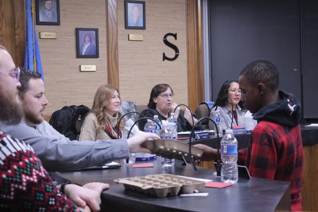 Tavion Hardeman, an eighth-grader at Jim Thorpe Academy, hands an egg carton to Casey White and other members of the Shawnee Board of Education during their meeting on Dec. 15. JTA Principal Hannah Holland reported on their Outdoor Classroom, which includes a chicken coop, tool shed, greenhouse and tiny house, all built by students and teachers. Holland invited the board members to bring their egg cartons to JTA for eggs in the future.