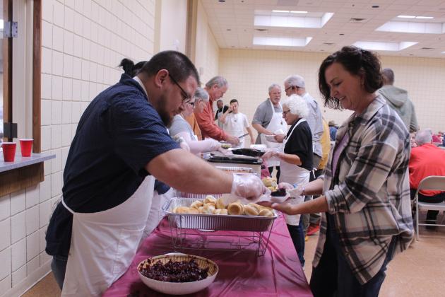 Volunteer Daniel Castaneda scoops cranberry sauce onto the plate of fellow volunteer Dustie Baker for her to serve to guests during the 20th Anniversary Tecumseh Family Thanksgiving Dinner, held at the Tecumseh City Hall Auditorium on Nov. 27. This is the first year for Castaneda, his wife Amber, and three daughters to volunteer at the event. Baker's parents, Randy and Suzanne Gilbert, began the dinner.